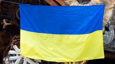 Ukrayna 'nın ulusal bayrağı harabelerin ve harap olmuş arabaların paslı metallerinin arka planına karşı. Ukrayna 'da savaş. Bombanın tahrip ettiği bir şehirde, güneşin altında dalgalanan mavi-sarı bir bayrak.