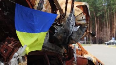 Ukrayna 'nın ulusal bayrağı harabelerin ve harap olmuş arabaların paslı metallerinin arka planına karşı. Ukrayna 'da savaş. Bombanın tahrip ettiği bir şehirde, güneşin altında dalgalanan mavi-sarı bir bayrak.