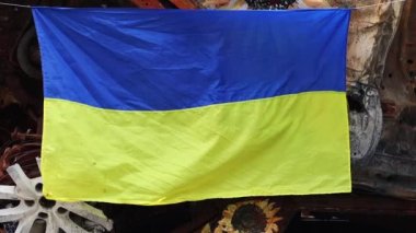 Ukrayna 'nın ulusal bayrağı harabelerin ve harap olmuş arabaların paslı metallerinin arka planına karşı. Ukrayna 'da savaş. Bombanın tahrip ettiği bir şehirde, güneşin altında dalgalanan mavi-sarı bir bayrak.