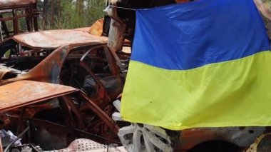 Ukrayna 'nın ulusal bayrağı harabelerin ve harap olmuş arabaların paslı metallerinin arka planına karşı. Ukrayna 'da savaş. Bombanın tahrip ettiği bir şehirde, güneşin altında dalgalanan mavi-sarı bir bayrak.