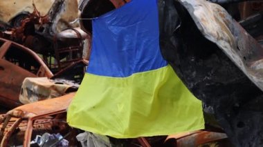 Ukrayna 'nın ulusal bayrağı harabelerin ve harap olmuş arabaların paslı metallerinin arka planına karşı. Ukrayna 'da savaş. Bombanın tahrip ettiği bir şehirde, güneşin altında dalgalanan mavi-sarı bir bayrak.