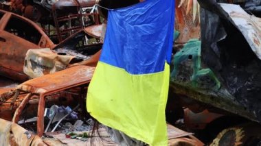 Ukrayna 'nın ulusal bayrağı harabelerin ve harap olmuş arabaların paslı metallerinin arka planına karşı. Ukrayna 'da savaş. Bombanın tahrip ettiği bir şehirde, güneşin altında dalgalanan mavi-sarı bir bayrak.