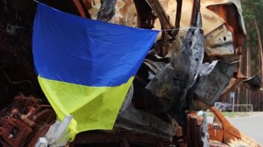 Ukrayna 'nın ulusal bayrağı harabelerin ve harap olmuş arabaların paslı metallerinin arka planına karşı. Ukrayna 'da savaş. Bombanın tahrip ettiği bir şehirde, güneşin altında dalgalanan mavi-sarı bir bayrak.