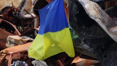 Ukrayna 'nın ulusal bayrağı harabelerin ve harap olmuş arabaların paslı metallerinin arka planına karşı. Ukrayna 'da savaş. Bombanın tahrip ettiği bir şehirde, güneşin altında dalgalanan mavi-sarı bir bayrak.
