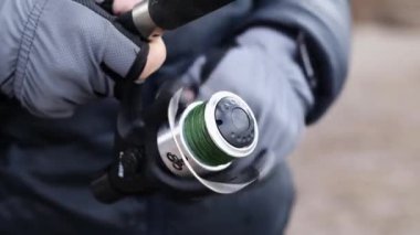 Elle dönen olta makarası, yavaş çekim. Bir adam nehirde ya da gölde balık tutar, balık tutmak için oltayı çeker. Yaşam tarzı kavramı, açık hava eğlencesi. Ukrayna, Kyiv - 5 Mart 2023