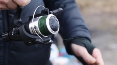 Balıkçı bir balık yakalar ve makarayı çevirir. Elinde olta kamışı olan bir balıkçının elleri yakın plan çekimde dönen makarayı kontrol ediyor ve ustalıkla sazan avlıyor. Ukrayna, Kyiv - 5 Mart 2023