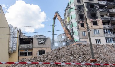 Çok katlı apartmanların yıkımı üzerine inşaat çalışması. Kırmızı ve beyaz uyarı bandından yapılmış. Konut binasının yıkımında hidrolik parçalayıcı ile kazıcı