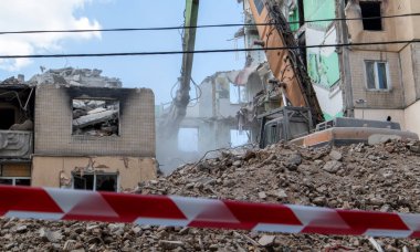 Çok katlı apartmanların yıkımı üzerine inşaat çalışması. Kırmızı ve beyaz uyarı bandından yapılmış. Konut binasının yıkımında hidrolik parçalayıcı ile kazıcı