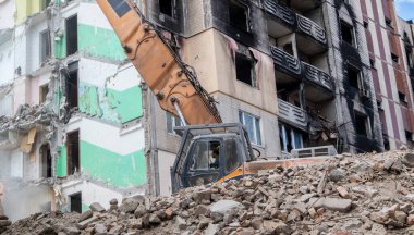 Şiddetli bir yangından sonra terk edilmiş çok katlı bir binanın ön cephesi. Hidrolik ezicisi olan bir inşaat kazıcısı tamir için bir evi yıkıyor. Bir yerleşim yerinin çökmesi.