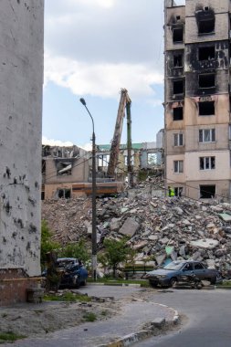 Şiddetli bir yangından sonra terk edilmiş çok katlı bir binanın ön cephesi. Hidrolik ezicisi olan bir inşaat kazıcısı tamir için bir evi yıkıyor. Bir yerleşim yerinin çökmesi.