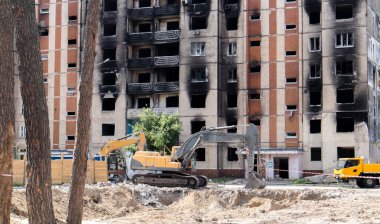 Şiddetli bir yangından sonra terk edilmiş çok katlı bir binanın ön cephesi. Hidrolik ezicisi olan bir inşaat kazıcısı tamir için bir evi yıkıyor. Bir yerleşim yerinin çökmesi.