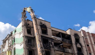 Şiddetli bir yangından sonra terk edilmiş çok katlı bir binanın ön cephesi. Hidrolik ezicisi olan bir inşaat kazıcısı tamir için bir evi yıkıyor. Bir yerleşim yerinin çökmesi.