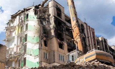 Şiddetli bir yangından sonra terk edilmiş çok katlı bir binanın ön cephesi. Hidrolik ezicisi olan bir inşaat kazıcısı tamir için bir evi yıkıyor. Bir yerleşim yerinin çökmesi.