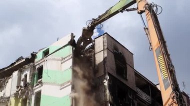 Konut binasının yıkımında hidrolik ezicili bir kazıcı. Şehir yenilenmesi. Parçalara ayırmak, çok katlı bir binayı yeniden inşa etmek için yıkmak. Enkaz temizleniyor.