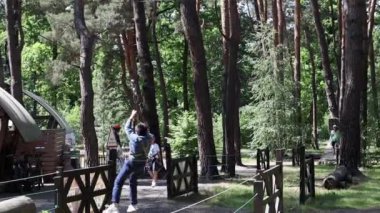 Küçük cesur bir çocuk parktaki ağaçların arasından bir halatla kayıyor. Spor macerası turizmi tecrübesi. Ukrayna, Kyiv - 28 Mayıs 2023