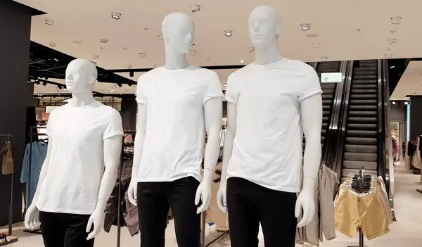 Showcase of a modern fashion store in a shopping center in the city center. Three mannequins in white t-shirts with copy space for your text