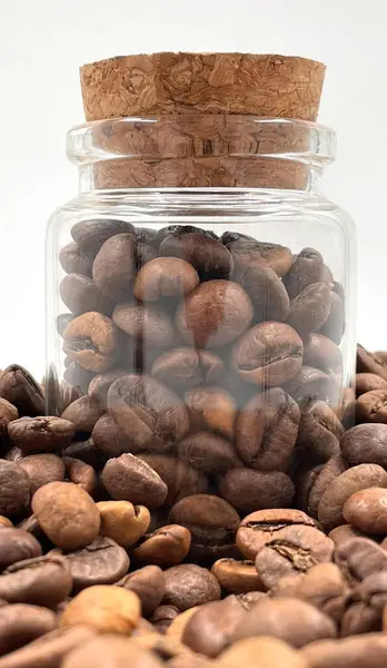 Coffee beans in a small glass jar with a cork lid on the table. Coffee beans packed in a transparent, airtight storage container. Coffee seeds inside a glass jar
