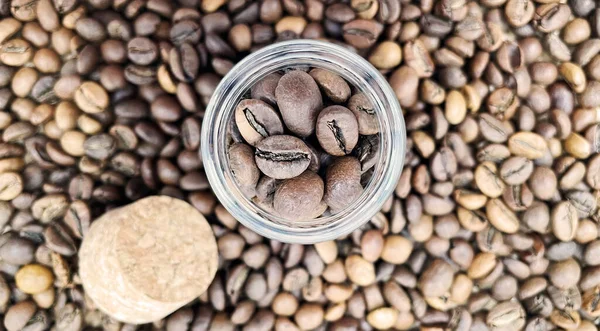 Coffee beans in a small glass jar with a cork lid on the table. Coffee beans packed in a transparent, airtight storage container. Coffee seeds inside a glass jar. Flat layout