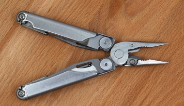 Ahşap zemin üzerinde gri demirden yapılmış modern, katlanmış, çok işlevli bir bıçak. Genişletilmiş alet ve kerpetenle çoklu alet. Küçük ve taşınabilir ürün. Çakı. EDC kavramı