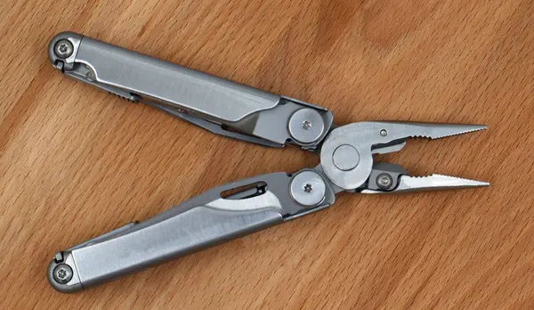 Ahşap zemin üzerinde gri demirden yapılmış modern, katlanmış, çok işlevli bir bıçak. Genişletilmiş alet ve kerpetenle çoklu alet. Küçük ve taşınabilir ürün. Çakı. EDC kavramı