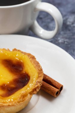 Bir Pastel de nata ya da Portekiz yumurtalı tart ve tarçınlı çubuk beyaz bir tabakta bir fincan kahve. Pastel de Belm çıtır börek hamurlu ve kremalı küçük bir turta.
