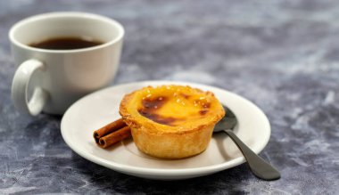 Bir Pastel de nata ya da Portekiz yumurtalı tart ve tarçınlı çubuk beyaz bir tabakta bir fincan kahve. Pastel de Belm çıtır börek hamurlu ve kremalı küçük bir turta.