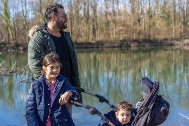 Babamın puset ve iki çocuğuyla Nehir Ormanı 'ndaki Aare nehri boyunca yürüdüğü yakın plan..