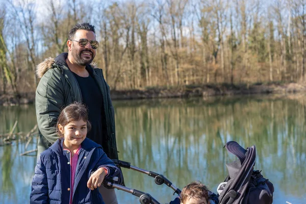 Close-up of father with stroller and two children walking along the Aare river in riparian forest in springtime.