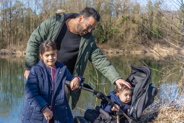 Close-up of father with stroller and two children walking along the Aare river in springtime.