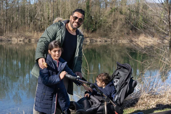 Father with stroller and two children is walking along the Aare river in springtime. Looking at camera.