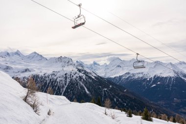 Two empty red chairlift in winter with rear side of mount matterhorn in background.