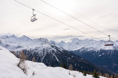 Focus on two empty red chairlift in winter with rear side of mount matterhorn in background.