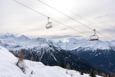 Two empty red chairlift in winter with rear side of mount matterhorn in background.