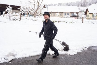 Neşeli bir baca temizleyicisi, temizleme aletlerini taşıyan, karla kaplı bir köy sokağında güvenle yürüyor. Huzurlu kış sahnesinde büyüleyici evlerin olduğu tuhaf kırsal bir ortam sergileniyor..