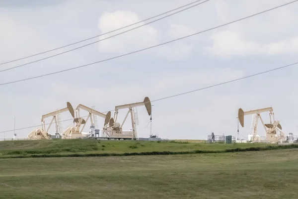 Several crude oil production wells, a site with pump jacks in a rural area during summer in Alberta Canada. Concept: Canadian oil and gas production.