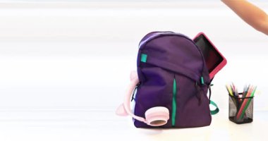 Bir öğrenci, içinde kulaklık, defter ve kalem kalemleri olan beyaz bir masada bir tablet bulunan okul çantası hazırlıyor. Konsept: Okulun temel ihtiyaçlarına dönüş