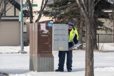 Calgary, Alberta, Kanada. 25 Şubat 2024. Bir postacı, kışlık koşullar altında mahalledeki bir posta kutusuna posta bırakıyor..