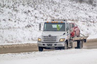 Calgary, Alberta, Canada. Mar 5, 2024. A towing company is pulling a car through the winter aftermath of a snowfall. clipart