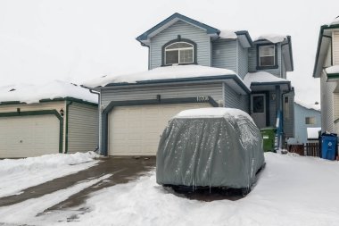 Calgary, Alberta, Kanada. Mar 5, 2024. Bir SUV dayanıklı gümüş bir araba kılıfına sarılır, kış boyunca garajın dışında kar tozu içinde oturur..