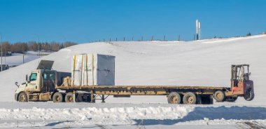 Calgary, Alberta, Kanada. Mar 6, 2024. Bir Flatbed Taşımacılık ve Ulaşım Hizmetleri yarı kamyoneti kış koşullarında inşaat malzemelerini etkili bir şekilde teslim ediyor..