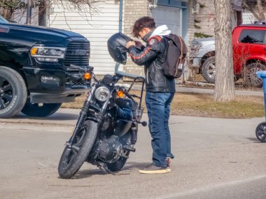 Calgary, Alberta, Kanada. 12 Nisan 2024. Motosikletine binmek için kaskını takmaya hazırlanan genç bir motosikletçi..