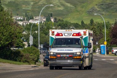 Calgary, Alberta, Kanada. 14 Temmuz 2024. Işıkları yanıp sönen ve sirenleri çalan bir ambulans, ıssız bir caddede ilerliyor..