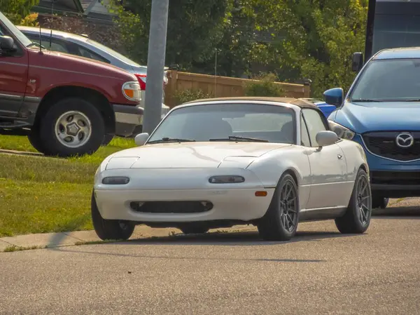 stock image Calgary, Alberta, Canada. Jul 17, 2024. A white Mazda MX-5 Miata parked on a suburban street, its compact and sporty design, features a soft-top roof and custom alloy wheels.