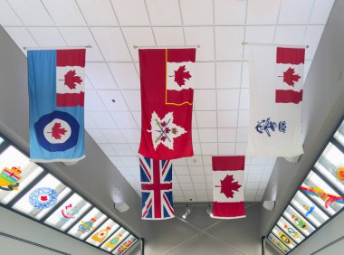 Calgary, Alberta, Kanada. 26 Haziran 2024. Kanada askeri ve İngiliz bayrakları da dahil olmak üzere çeşitli bayraklar, iyi aydınlatılmış bir koridorda, amblem ve simgelerle süslenmiş bir tavandan sarkıyor..