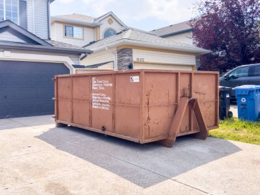 Calgary, Alberta, Kanada. Ağustos 5, 2024. Paslı bir çöp konteynırı konutun garajında duruyor. Çöp konteynırının yan tarafında yasaklı öğelerin bir listesi var.