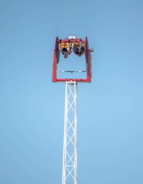 Calgary, AB, Kanada. 12 Temmuz 2024. Gökdelen 'in doruk noktasında olduğu heyecan verici bir lunapark. Süvariler açık mavi gökyüzüne karşı kırmızı ve sarı bir kapsülde baş aşağı asılı duruyor..
