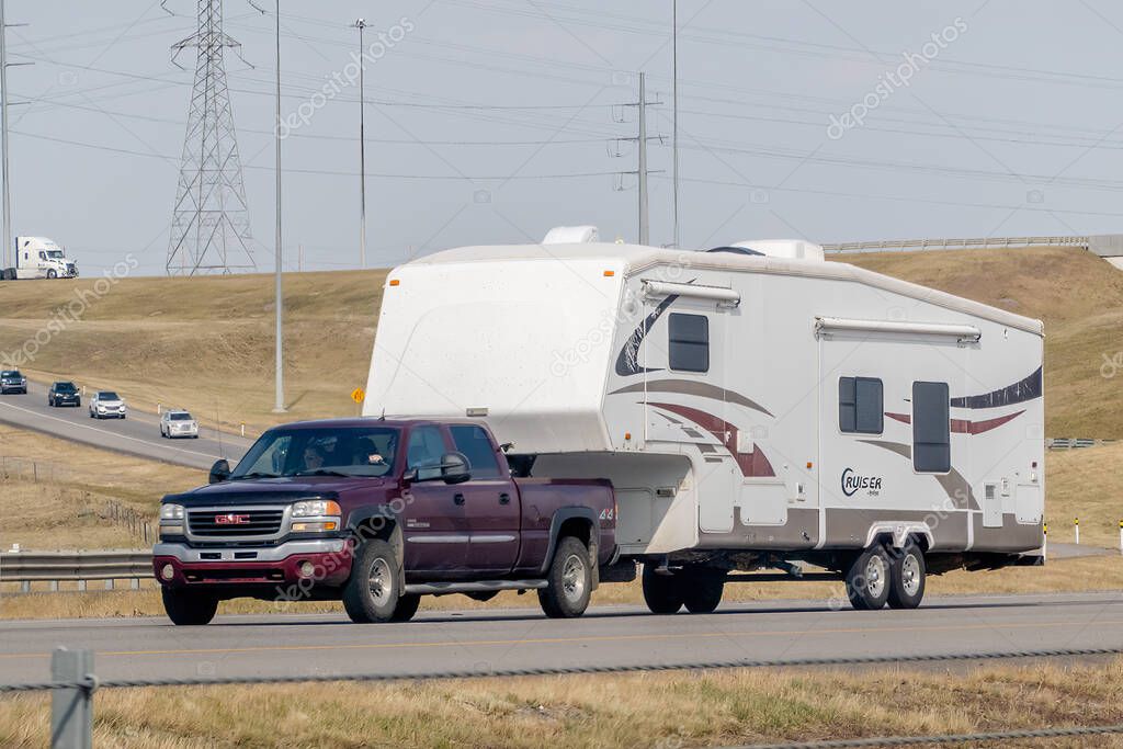 Calgary, Alberta, Canada. Aug 12, 2024. A maroon GMC Sierra HD truck towing a white fifth-wheel RV labeled 