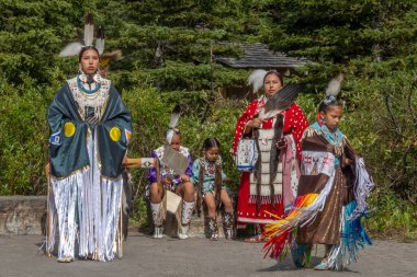 Louise Gölü, AB, Kanada. 27 Ağustos 2024. İlk Milletler 'den bir grup canlı, geleneksel regalia' lı insan açık havada duruyor. Her bir birey, ormandaki bir tüy ve boncukta karmaşık boncuklar sergiliyor..
