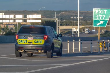 Calgary, AB, Kanada. 26 Ağustos 2024. Çıkış rampasının yakınındaki otoyolda güvenli mesajı olan bir polis aracı beyaz korkulukların arkasında ve kalabalık yolda araçlarla çevrili..