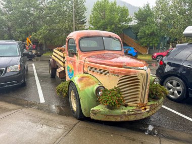 Waterton Park, AB, Kanada. 22 Ağustos 2024. Renkli çiçeklerle süslenmiş klasik bir REO Speedwagon kamyonu ıslak bir sokakta duruyor. Kamyonun dışı yıpranmış ve canlı çiçek aranjmanı var..